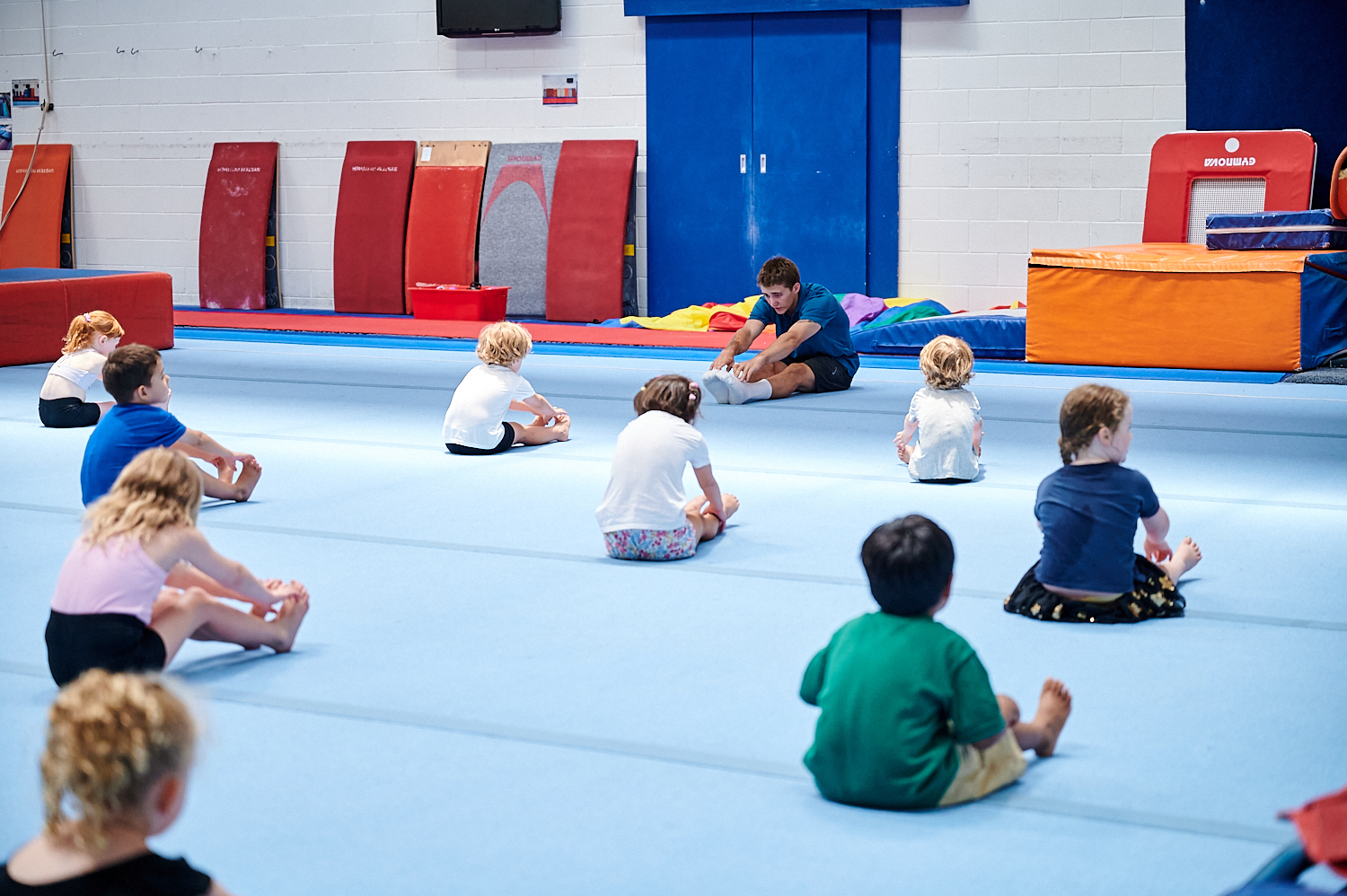 A group of kids spread out on the floor mats doing guided stretching at Perth HPC Kids Gym class