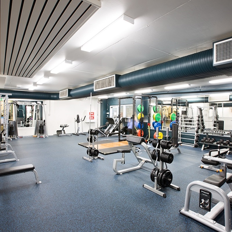 A photo of a floor space in a gym with free weights and machines spread out around the room